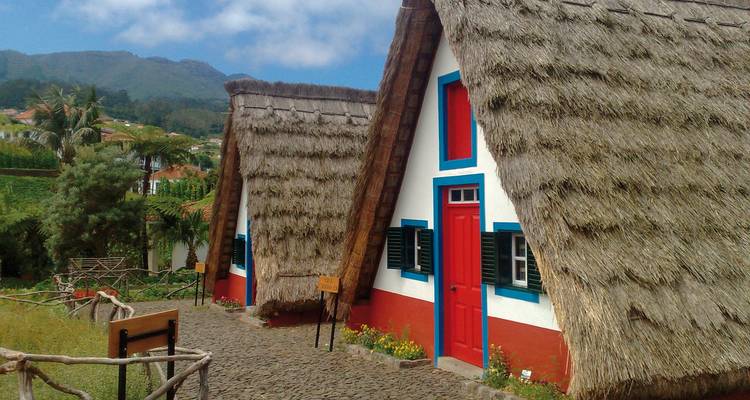 Maisons traditionnelles au toit de chaume triangulaire dans un cadre rural.
