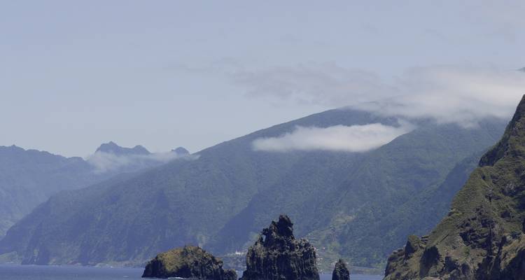 Falaises rocheuses sur un fond de montagnes verdoyantes et d'océan.