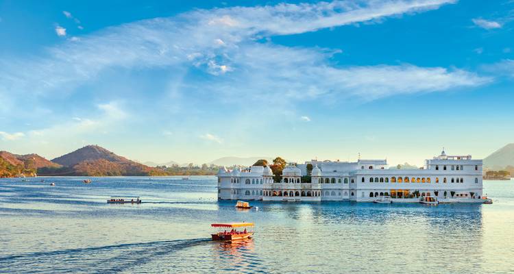 Wunderschöner weißer Palast an einem ruhigen See mit umliegenden Hügeln unter strahlend blauem Himmel.