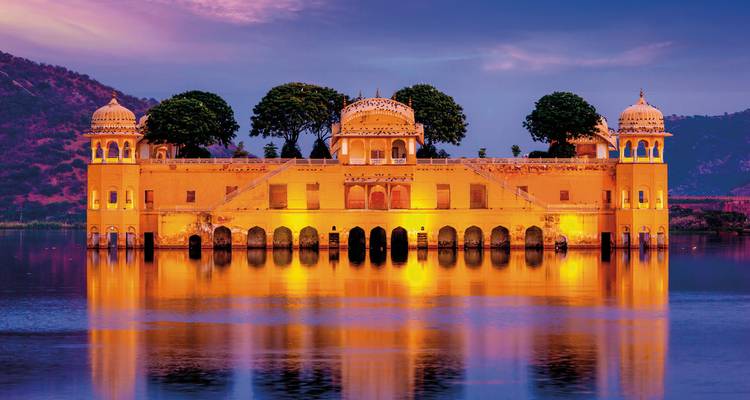 Jal Mahal Palast in der Mitte eines Sees mit einer malerischen Kulisse von Hügeln bei Sonnenuntergang.