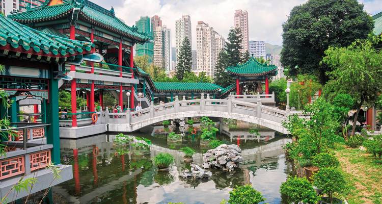Traditional Chinese garden with a bridge and modern buildings in the background.