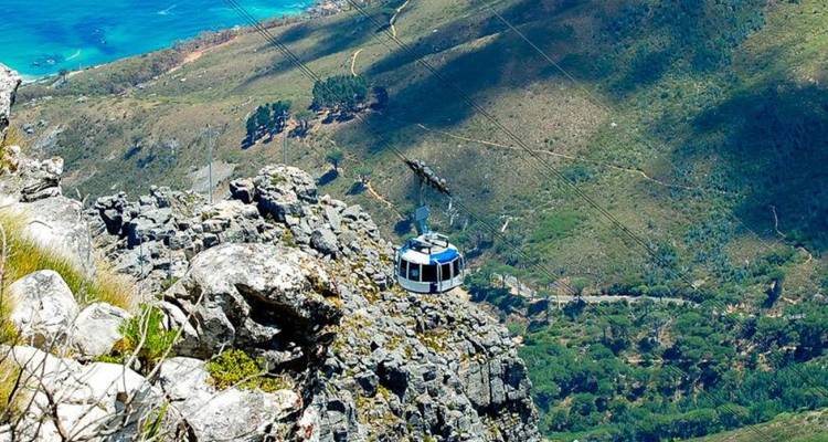 Cable car ascending rocky mountain landscape.