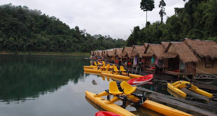 Bungalows op palen aan een meer met waterfietsen.