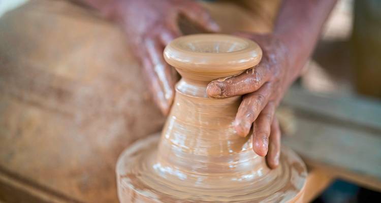 Nahaufnahme von Händen, die an einer Töpferscheibe arbeiten und Ton formen.