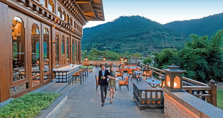 Außenterrasse mit Essbereich, zwei Personen gehen vorbei, vor Bergkulisse.