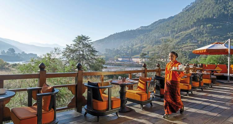 Hotelterrasse mit einer Person, die ein Tablett trägt, mit Bergen im Hintergrund.