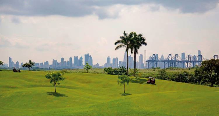 Green golf course with a view of Panama City skyline in the distance.