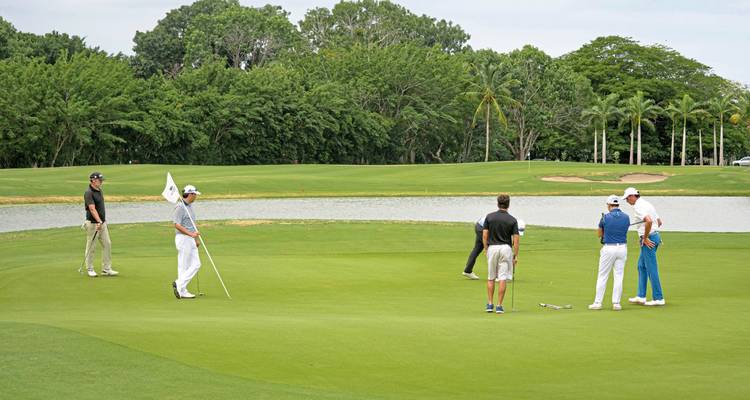 Golfers standing on a green field, discussing play strategy.
