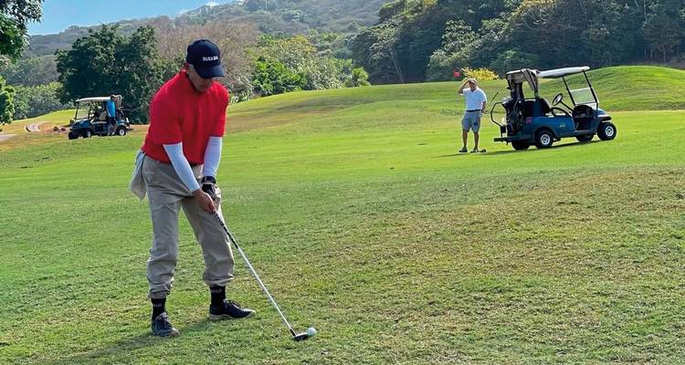 Golfer preparing to swing on a grassy course with trees in the background.