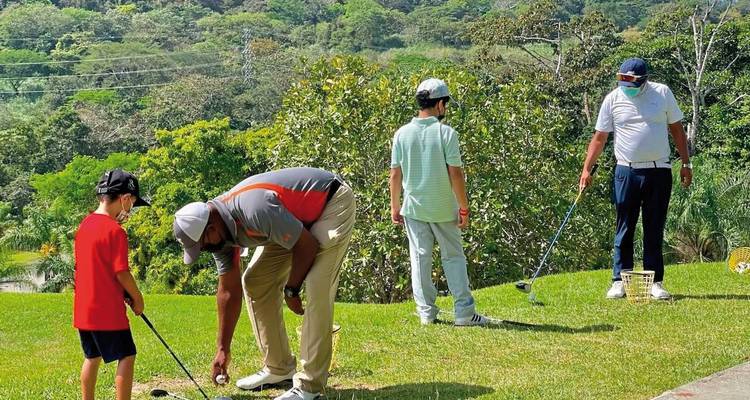 Group of people practicing golf on a lush green course.