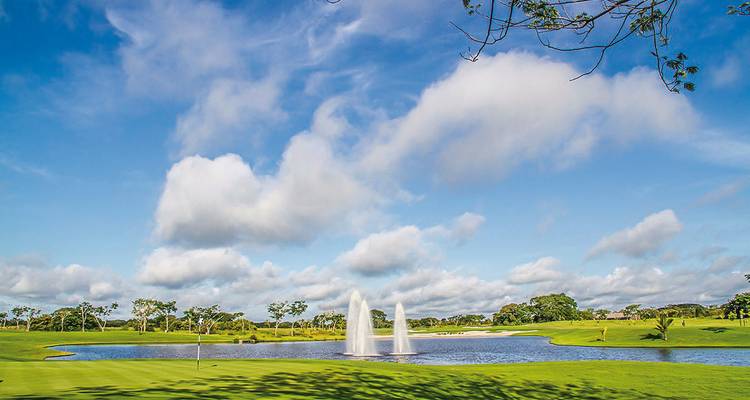 Golf course with a fountain in a pond under a bright blue sky.