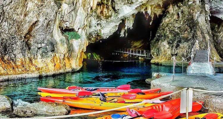 Colorful sea kayaks float beside a dramatic cave entrance with clear turquoise water.