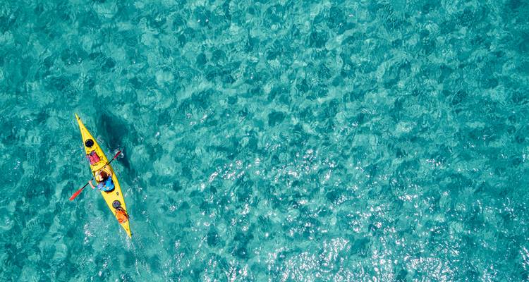 Drone view of a tandem kayak gliding over crystal-clear azure sea.