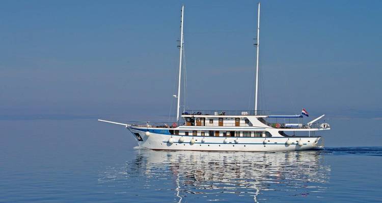 Yacht segelt auf ruhigen blauen Gewässern unter klarem Himmel.
