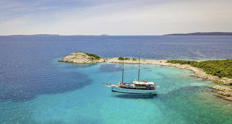 Sailing vessel anchored in a turquoise bay surrounded by small islands.