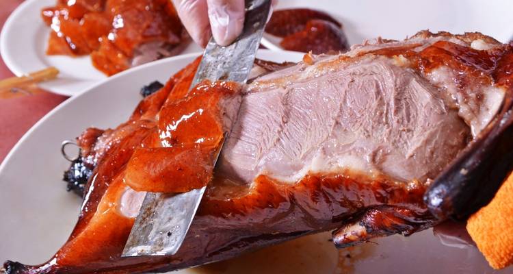 Close-up van een gebraden eend die wordt gesneden met een groot mes.