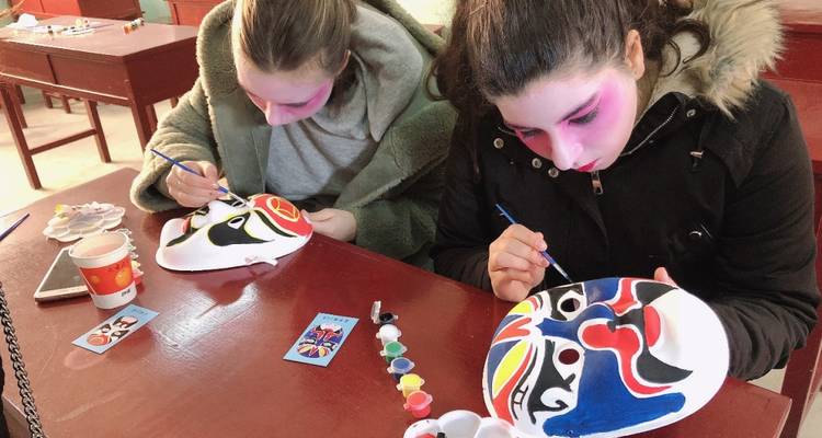 Twee mensen die traditionele maskers met kleurrijke ontwerpen schilderen in een werkplaats.