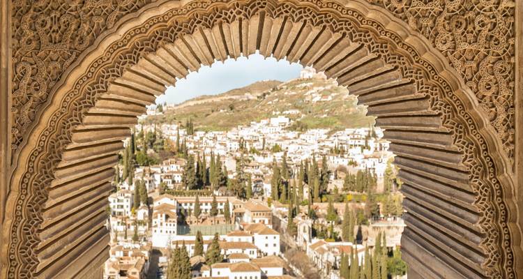Blick durch einen verzierten Torbogen auf eine Hügelstadt.