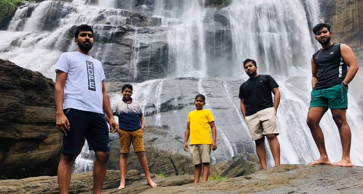 Five people standing on rocks with a large waterfall behind them.