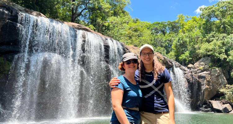 Two women smiling in front of a waterfall.
