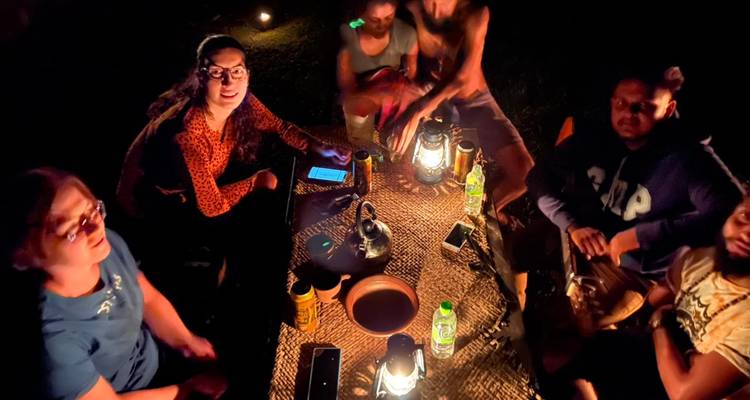 Group of people seated outdoors around a table illuminated by lanterns at night.