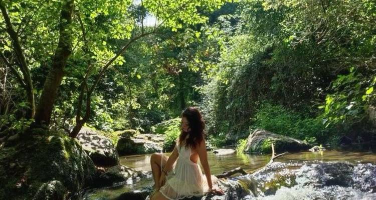 Femme assise sur des rochers près d'un ruisseau dans une forêt luxuriante.