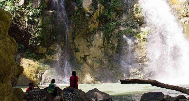 Des gens assis près d'une grande cascade avec des inscriptions sur les rochers.