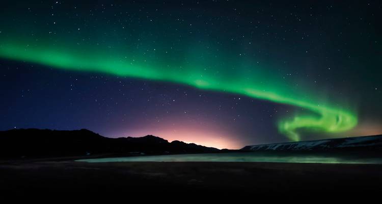 Grüne Nordlichter über einer verschneiten Landschaft mit Hügeln.