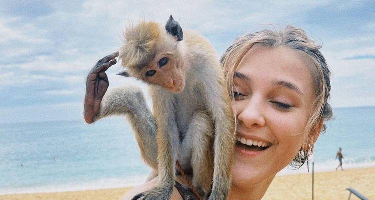 Person with a monkey on their shoulder by the beach.