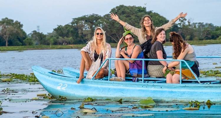 Group of women on a blue boat in a lake, surrounded by greenery.