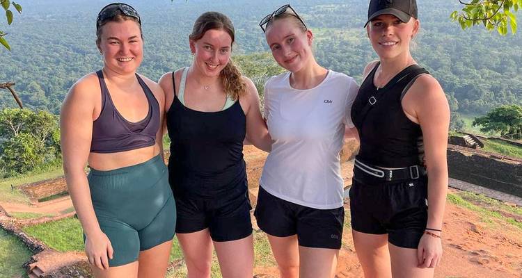 Four women posing at a viewpoint with scenic forest behind them.