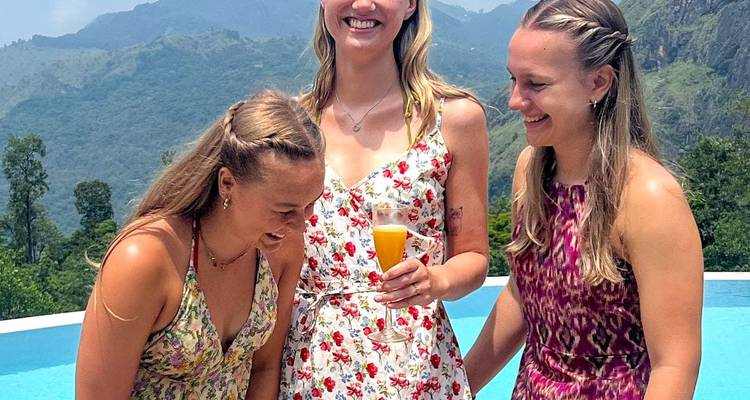 Three women at a poolside with mountains in the background.