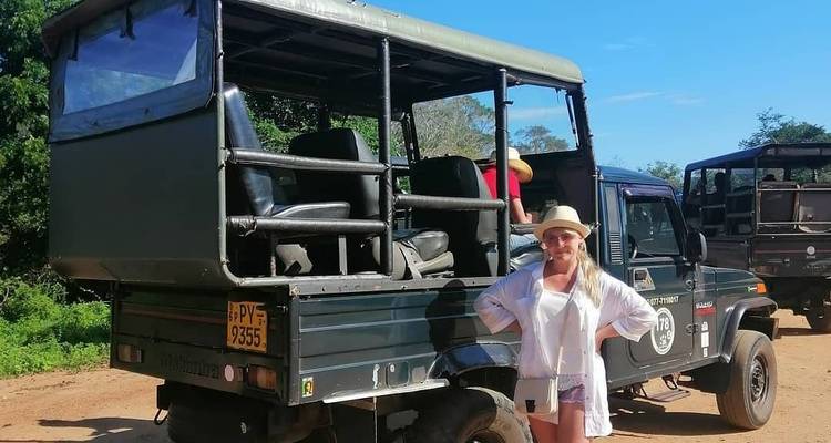 Woman standing next to a safari vehicle with a blue sky background.