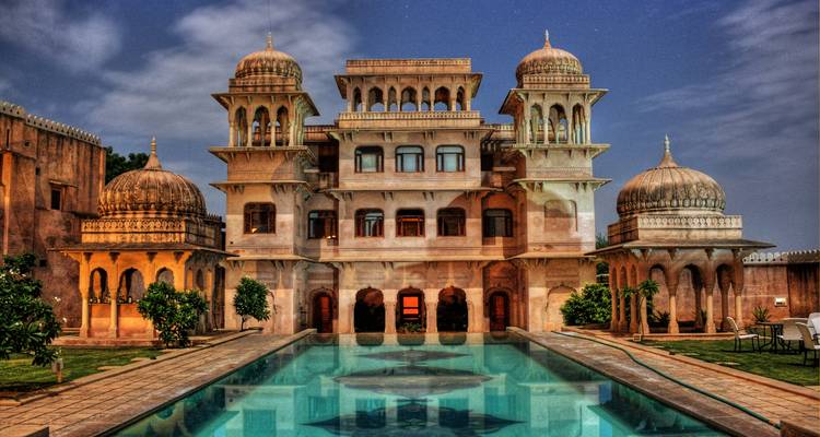 Prächtiger Palast mit Kuppeln und Säulen, der sich nachts in einem Wasserbecken spiegelt.