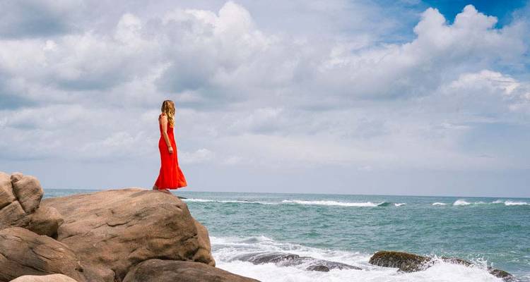 Woman in a red dress standing on rocks by the sea