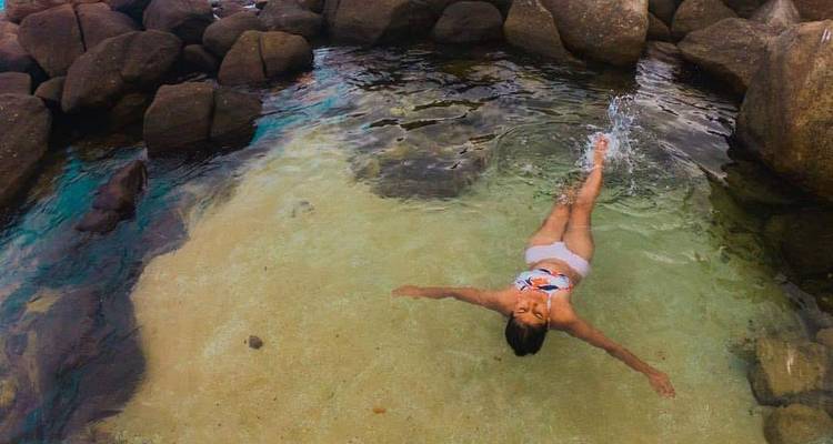 Une personne flottant dans une piscine d'eau claire entourée de rochers.