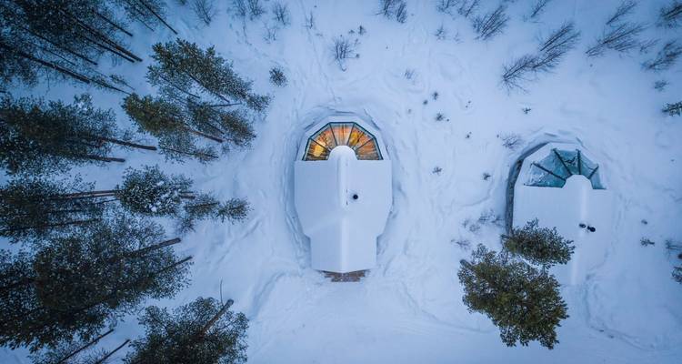 Aerial view of snow-covered cabins surrounded by trees.