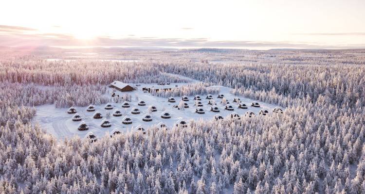 Une vue aérienne d'un paysage enneigé avec des structures semblables à des igloos et une forêt au coucher du soleil.