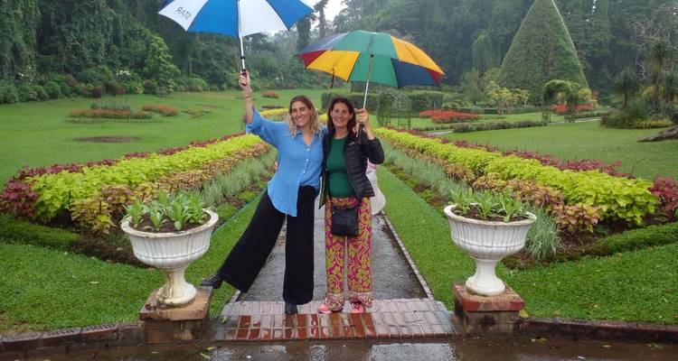 Deux femmes debout avec des parapluies dans un jardin luxuriant.