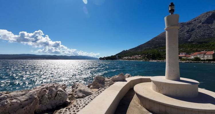 Bright seaside scene with a small white lighthouse column overlooking sparkling Adriatic water