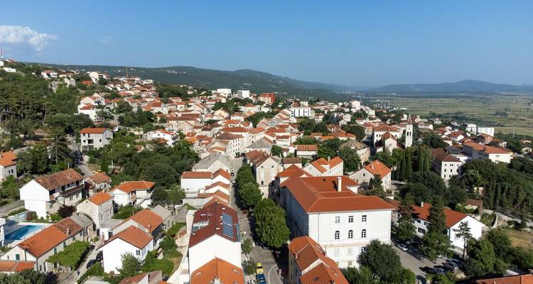 Aerial view of a Croatian inland town with red-tiled roofs surrounded by green hills