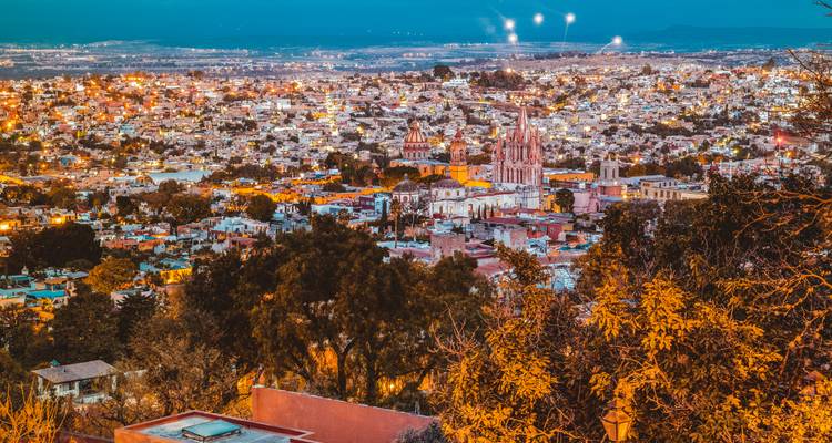 Nighttime panoramic view of a city with twinkling lights and church towers.