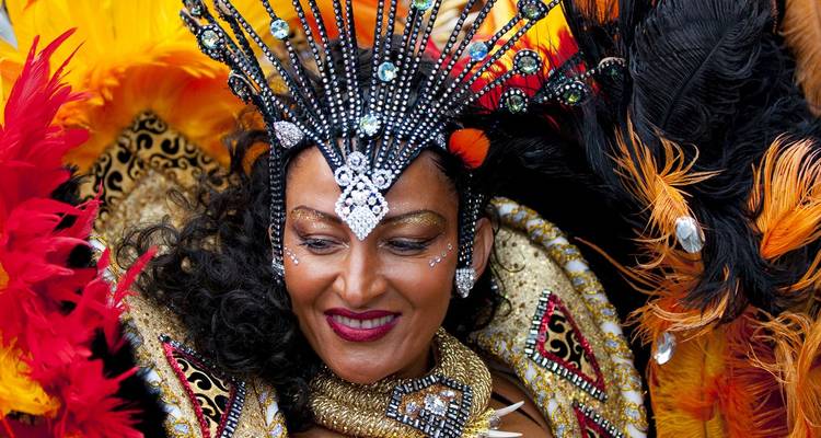 Femme souriante vêtue d'un costume de carnaval éblouissant avec un diadème orné de bijoux et de plumes aux couleurs éclatantes.