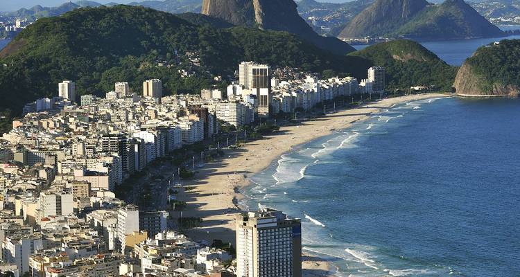 Vue aérienne de la plage de Copacabana bordée de gratte-ciel, de vagues bleues de l'Atlantique et de montagnes boisées au-delà.