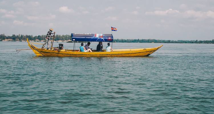 Pequeña barca de madera amarilla con la bandera camboyana llevando turistas a través de aguas tranquilas del río