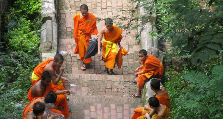 Moines en robes orange assis sur des escaliers extérieurs.