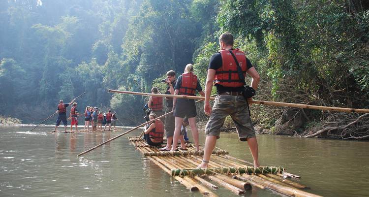 Reizigers manoeuvreren bamboe vlotten over een rustige rivier in de jungle terwijl ze reddingsvesten dragen.