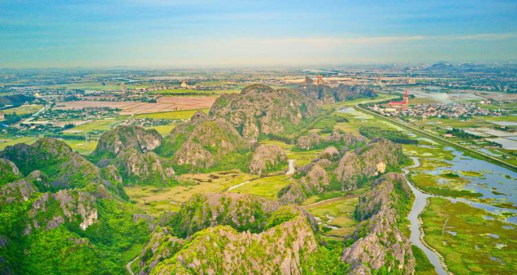 Vue aérienne de karsts calcaires et de champs luxuriants sous un ciel bleu.