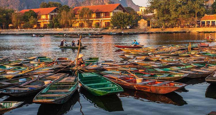 Dozens of small rowboats cluster on a reflective river beside traditional buildings at sunset in Ninh Binh.