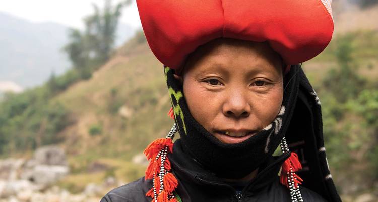 Portrait of an ethnic minority woman wearing a vibrant red headdress and patterned scarf.